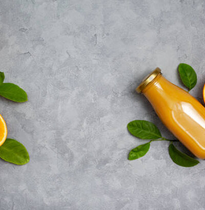 Orange juice in a glass bottle, fresh oranges on a gray background.