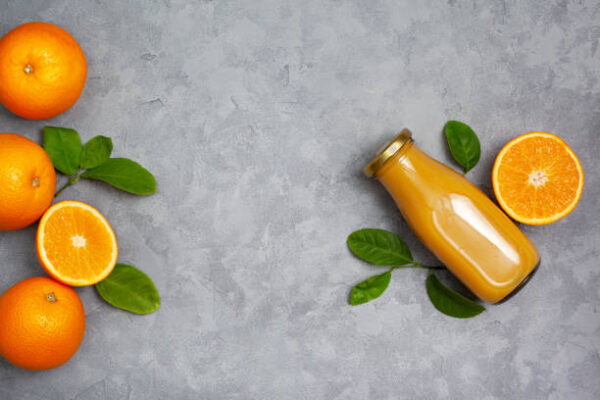 Orange juice in a glass bottle, fresh oranges on a gray background.