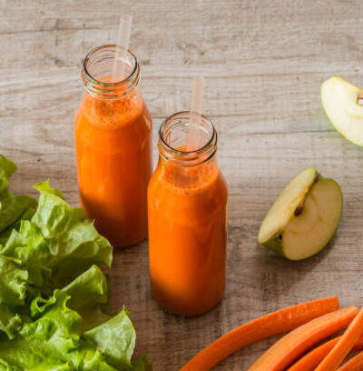 Fresh carrot juice in bottles on a grey wooden table.