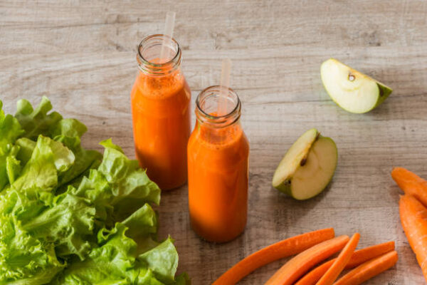 Fresh carrot juice in bottles on a grey wooden table.